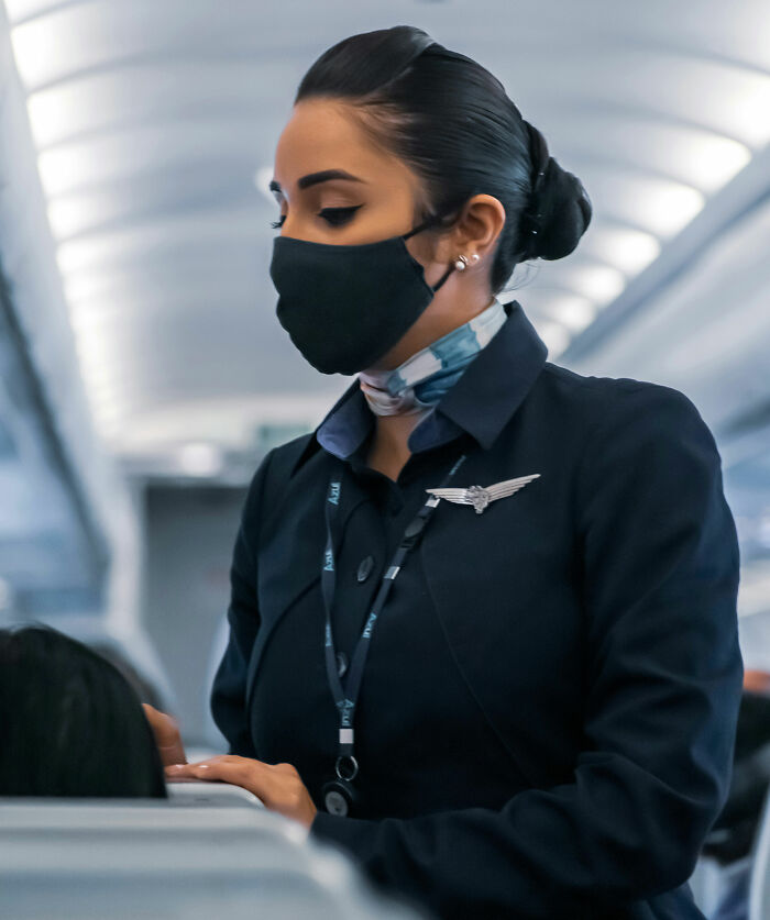 A flight attendant wearing a face mask and uniform, highlighting things a passenger could do.