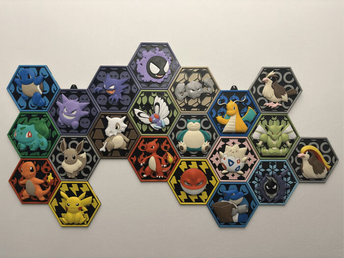 A wall display of various 3D printed Pokemon characters set in hexagonal tiles, showcasing fun 3D printer creations.