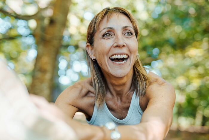 A happy middle-aged woman laughing outdoors, experiencing positive body changes in her 30s and 40s.