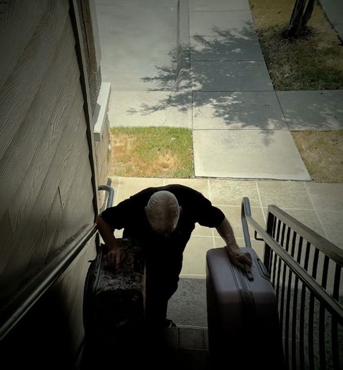 An 81-year-old dad carrying heavy suitcases up concrete stairs An 81-year-old dad carrying heavy suitcases up concrete stairs