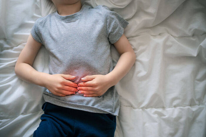 A child lies in bed, holding their stomach, indicating extreme illness and sickness.
