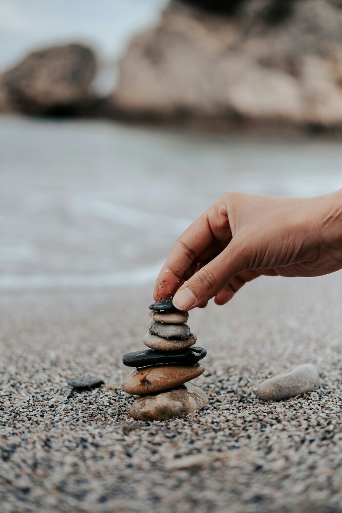 A hand carefully stacking small stones on a sandy beach, illustrating childhood beliefs.