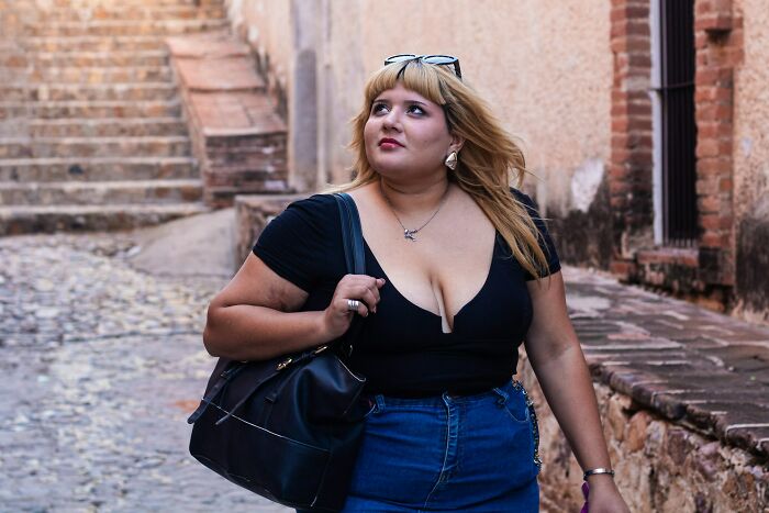 Blonde woman in black top and jeans walking outdoors, experiencing body changes in her 30s.