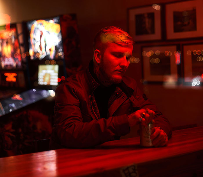 Man alone at bar in red light reflecting on drinking problem warning signs Man alone at bar in red light reflecting on drinking problem warning signs