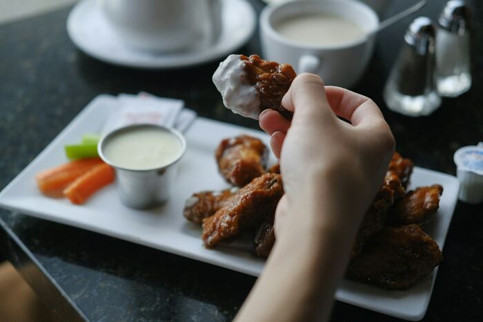 A hand holding a chicken wing dipped in sauce, part of a collection of stupid things people said.