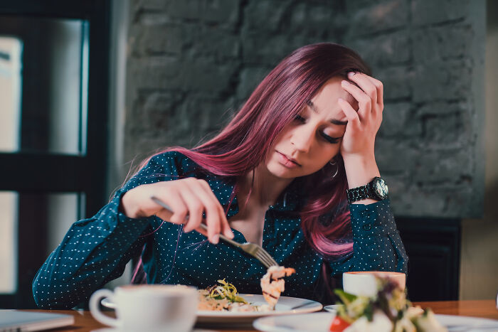 A woman with pink hair looking bored and awkward during a first date while eating a meal.