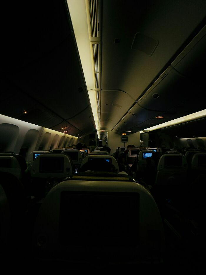 Dark airplane cabin during a night flight, showing rows of seats and overhead compartments. Cabin crew deal with passenger needs.
