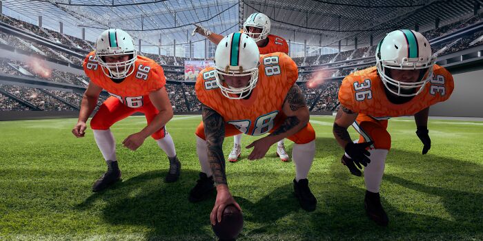 Football players in orange and white uniforms line up on a field, ready for a play, illustrating surprising things wealthy people buy.