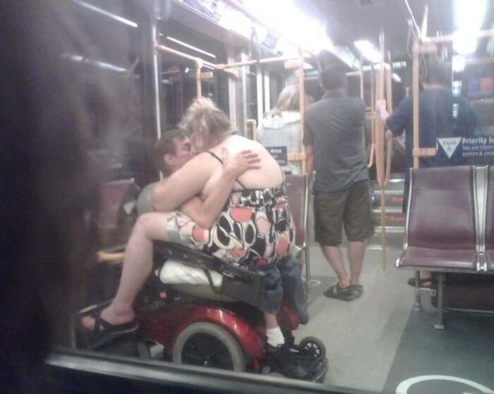 A couple kissing passionately on a mobility scooter inside a public transport vehicle