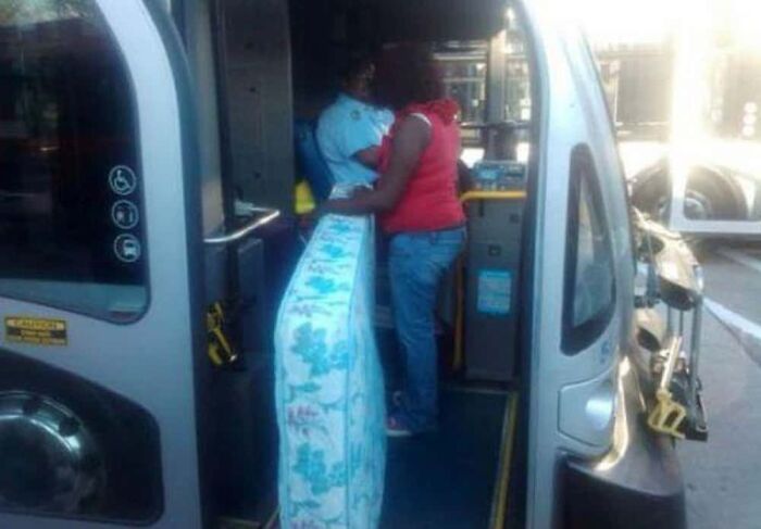 A woman trying to load a mattress onto a bus, an unusual public transport interaction.