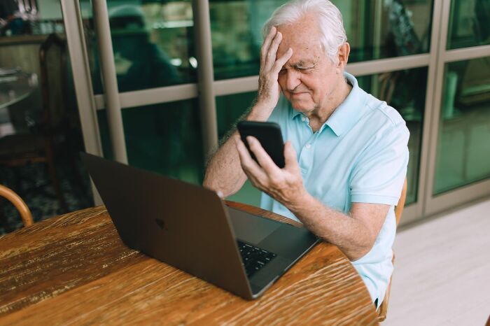 Elderly man looking at phone with a frustrated expression, experiencing an everyday inconvenience.