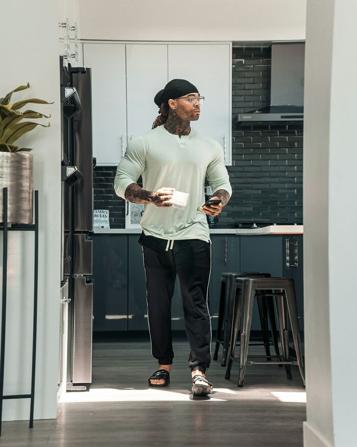 A man with dreadlocks, glasses, and tattoos in a kitchen, experiencing everyday inconveniences.
