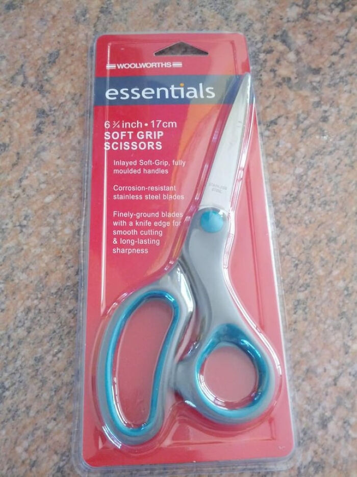 A pair of Woolworths Essentials soft grip scissors in red packaging, illustrating everyday inconveniences that most people cant avoid.