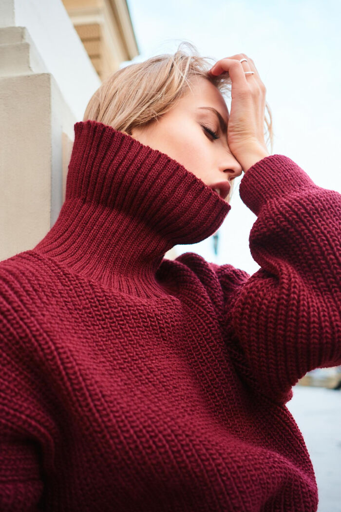 A woman in a red turtleneck sweater holds her head, frustrated by an everyday inconvenience.