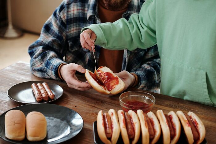 Two people preparing hot dogs with ketchup, showcasing funny descriptions of everyday inconveniences.