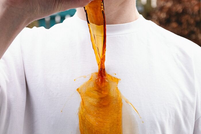 A person spills a drink on a white t-shirt, illustrating an everyday inconvenience.