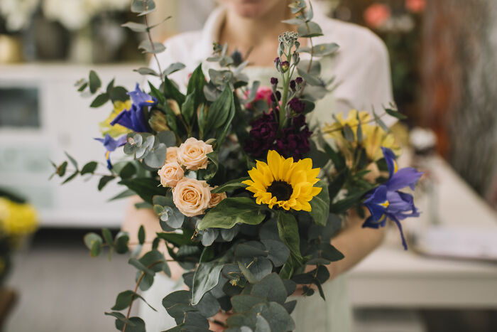 A person holds a vibrant bouquet of flowers, including sunflowers and roses, showcasing surprising things wealthy people buy.