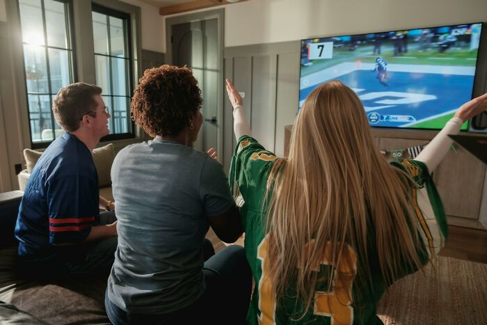 A group of friends watching sports on TV, with one person enthusiastically raising their arms, showing things people said.