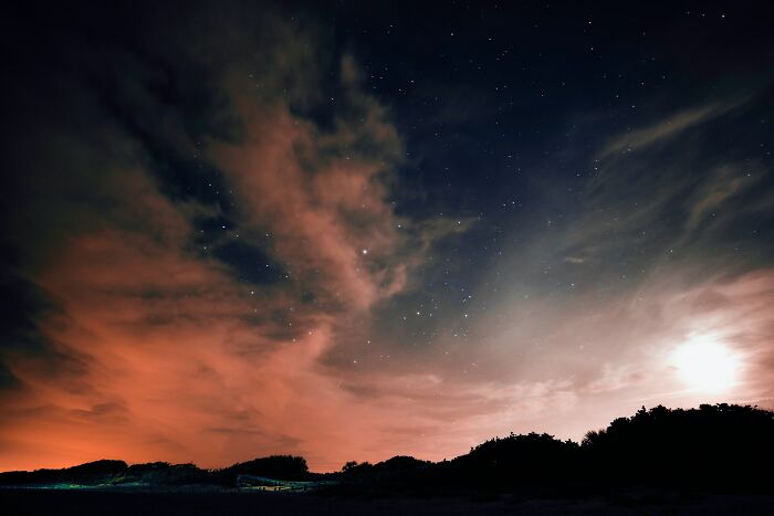A dramatic night sky with orange-lit clouds and stars over a dark landscape, illustrating cool facts about the universe.