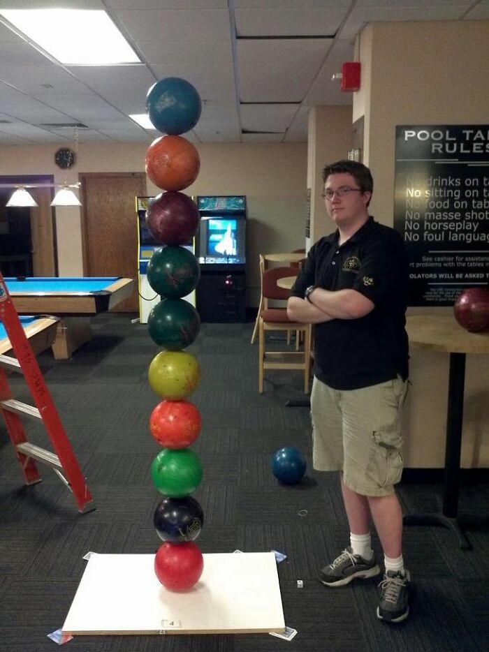 A baffling image of a man standing next to an impossibly tall stack of bowling balls, defying physical sense.