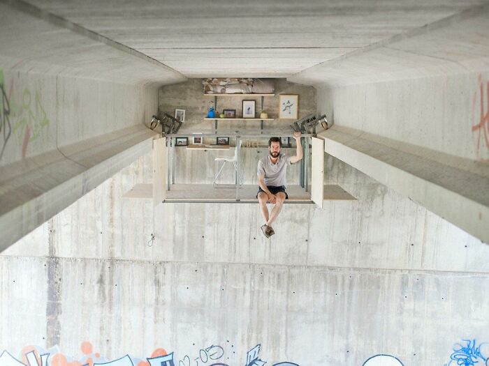 A man sitting on a suspended platform under a concrete bridge, a baffling image that defies physical sense.