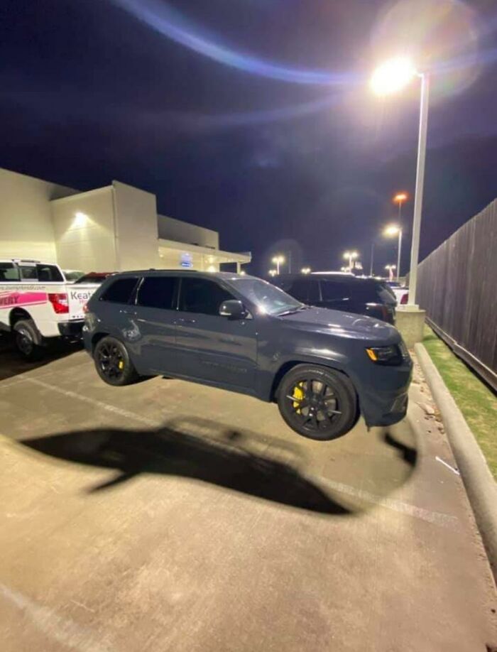 A baffling image of a floating gray SUV in a parking lot at night, defying physical sense.