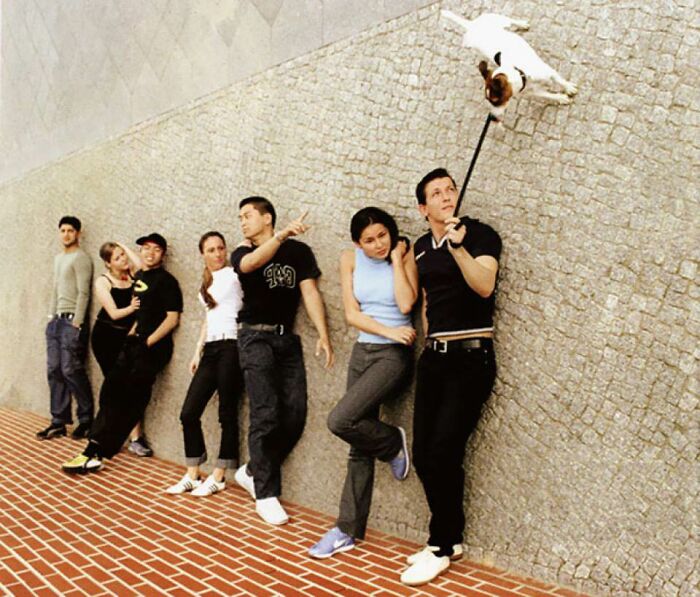 A group of people standing against a wall, with a dog seemingly floating from a leash, a baffling image.