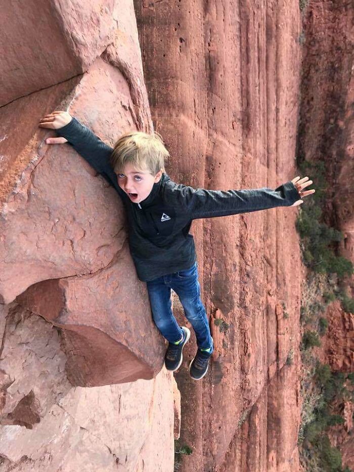 A baffling image of a young boy with arms outstretched, seemingly clinging to a red rock cliff face, defying physical sense.