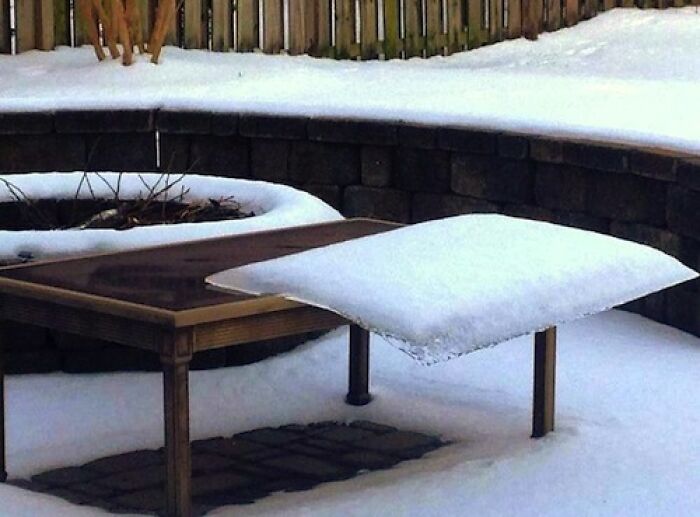 A baffling image of snow forming a perfect, elevated square layer over a table in a snowy backyard, making no physical sense.