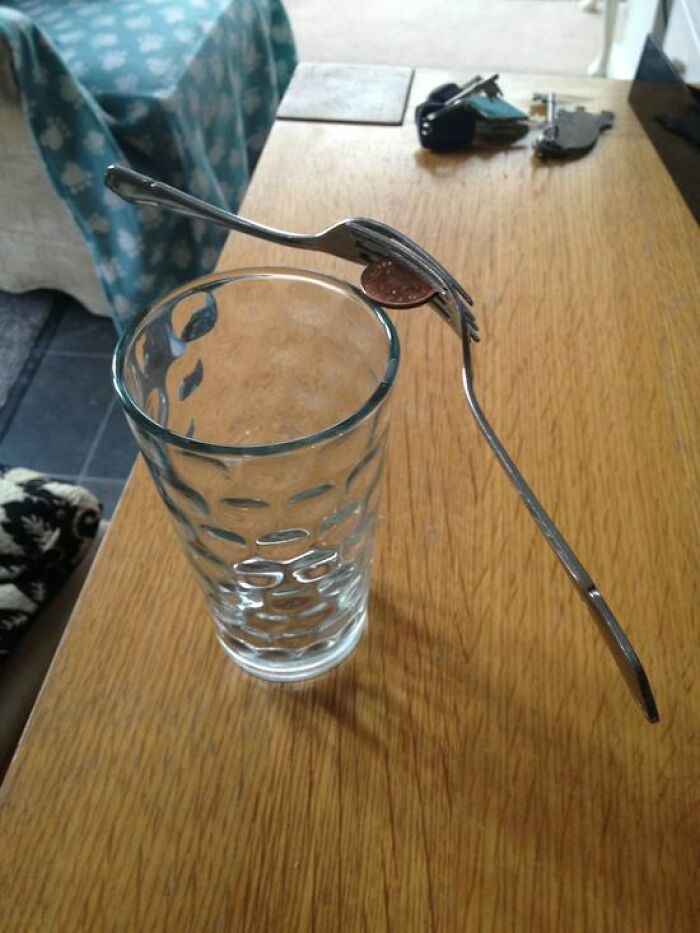 A baffling image of two forks balancing a coin on the rim of a glass, appearing to defy physical sense.