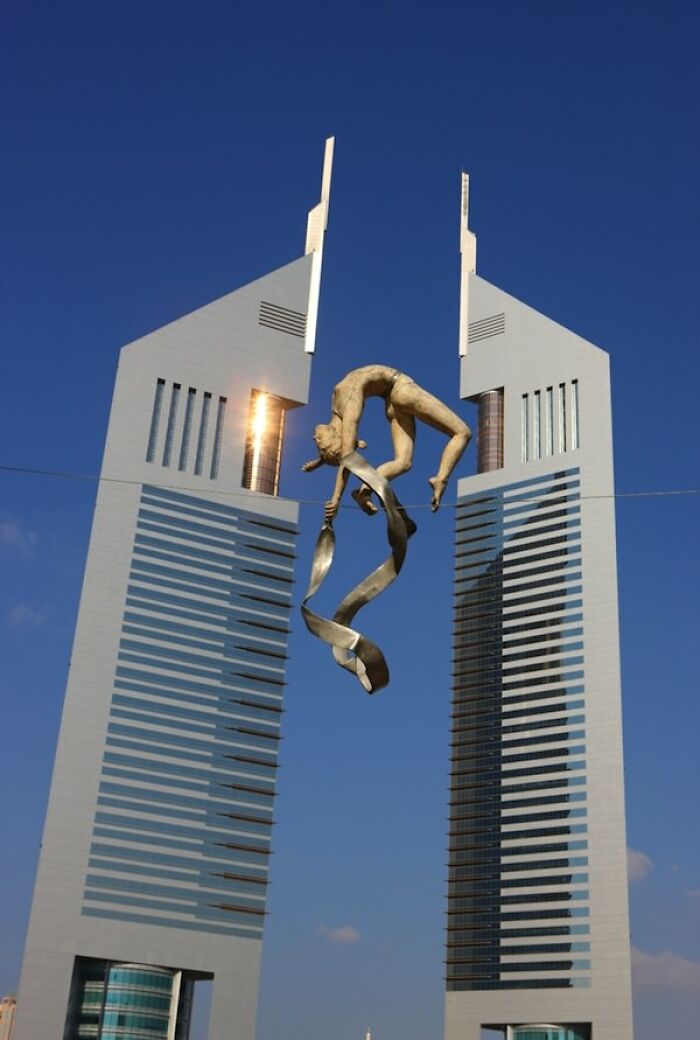 A gravity-defying statue of a woman doing acrobatics between two tall buildings, a truly baffling image.