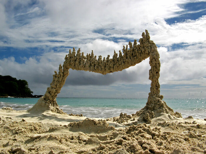 A surreal sand sculpture shaped like an arch on a beach, a baffling image that seems to defy gravity.
