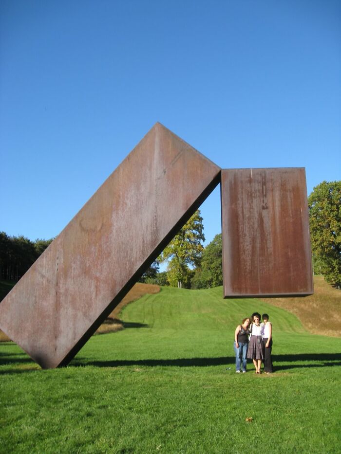 A baffling image of three people standing next to two massive, seemingly precariously balanced metal slabs, defying physical sense.