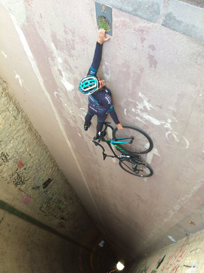 A baffling image of a cyclist and bike clinging to a vertical wall, defying physical sense.