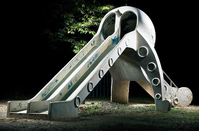 A surreal Japanese playground at night with a unique, weathered concrete slide design, by Fujio Kito.