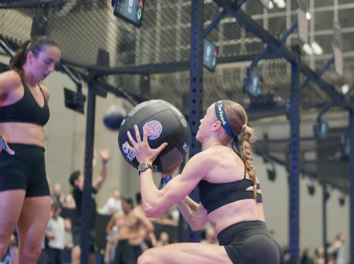 A HYROX athlete performing a wall ball exercise with a medicine ball during the race, demonstrating strength and commitment.