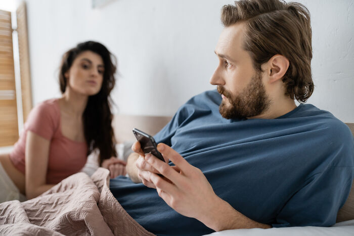 A concerned woman looks at a man using his phone, showing why some divorced people lose trust