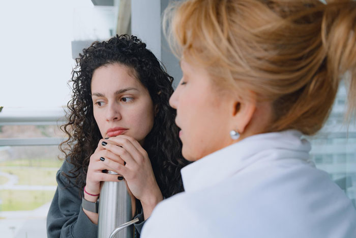 A woman with curly hair looking thoughtful while another person speaks, relating to a bride trying to get a love confession from the groom's female bestie. A woman with curly hair looking thoughtful while another person speaks, relating to a bride trying to get a love confession from the groom's female bestie.