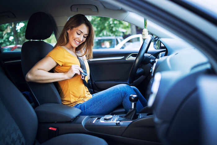 A smiling woman buckles her seatbelt in a car, an action that prevents serious issues and illustrates the innocent beginning of safety.