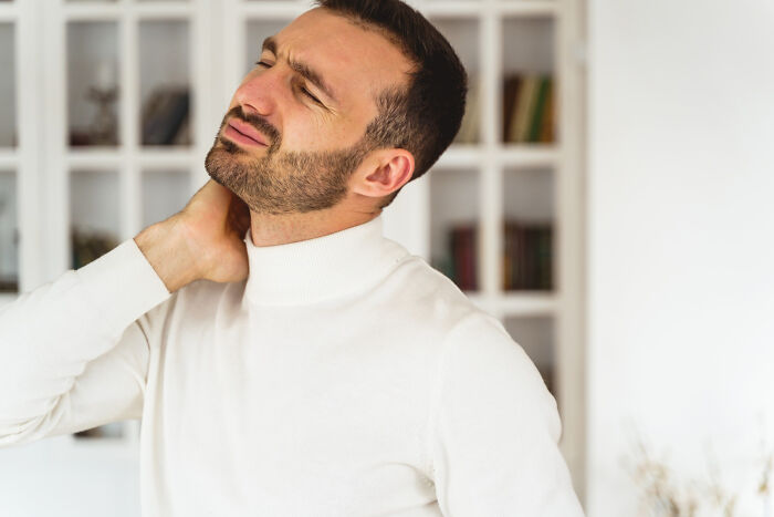 Man in a white turtleneck rubbing his neck in pain, representing medical professionals treating serious issues.