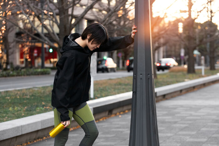 Woman in athletic wear leaning on a pole, looking unwell, symbolizing serious issues that started seeming innocent.