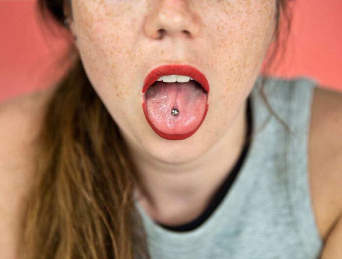 Close-up of a woman's mouth with red lipstick and a tongue piercing, highlighting how seemingly innocent things can lead to serious issues.