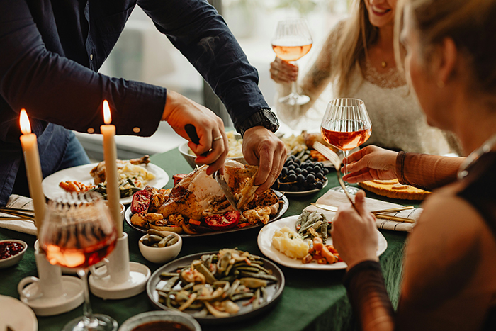 A man carving turkey at a festive dinner, representing Thanksgiving with the host serving guests. A man carving turkey at a festive dinner, representing Thanksgiving with the host serving guests.