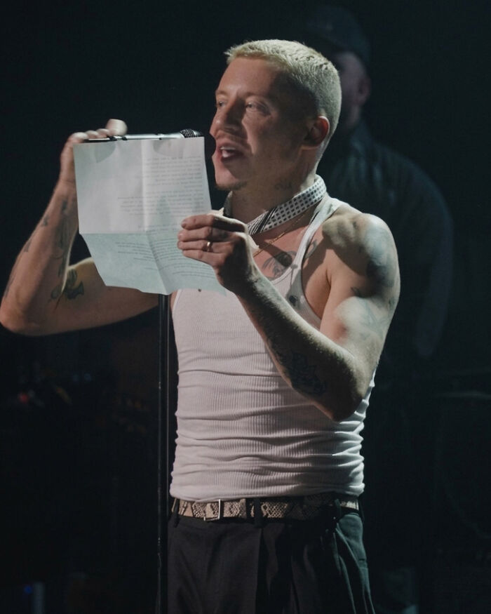 Macklemore reads from a paper on stage, relating to his removal from the Ed Sheeran tour.