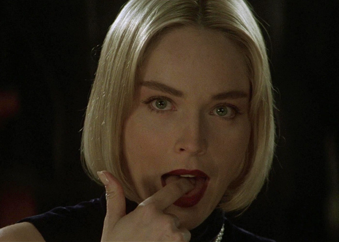 Actress Sharon Stone in a blonde bob, licking her finger, in a scene from a film.