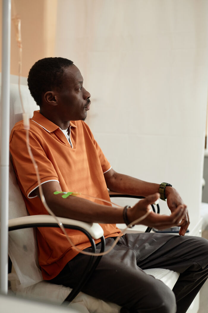 An African American man with an IV drip in his arm, experiencing extreme illness and sickness.