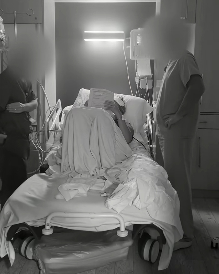 Black and white image of a woman obscured by a sheet in a hospital bed with medical staff around, after recent childbirth. Black and white image of a woman obscured by a sheet in a hospital bed with medical staff around, after recent childbirth.