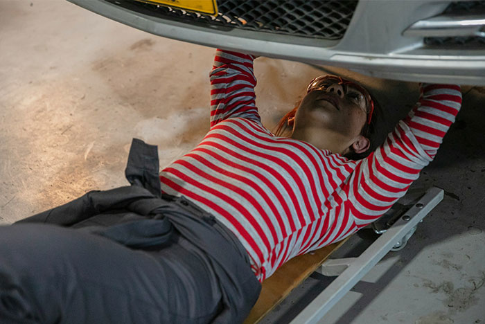 A woman looking under her vehicle where a nanny finds AirTag in her car