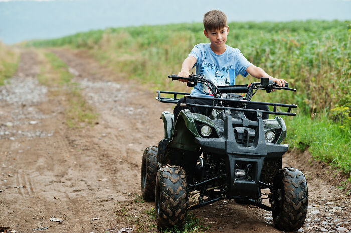 A young boy on an ATV on a dirt path, showing a pain reaction after an accident.