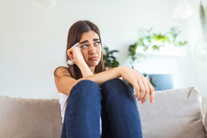 A crying woman sitting on a couch, feeling stressed about her jobless BF who needs financial advice